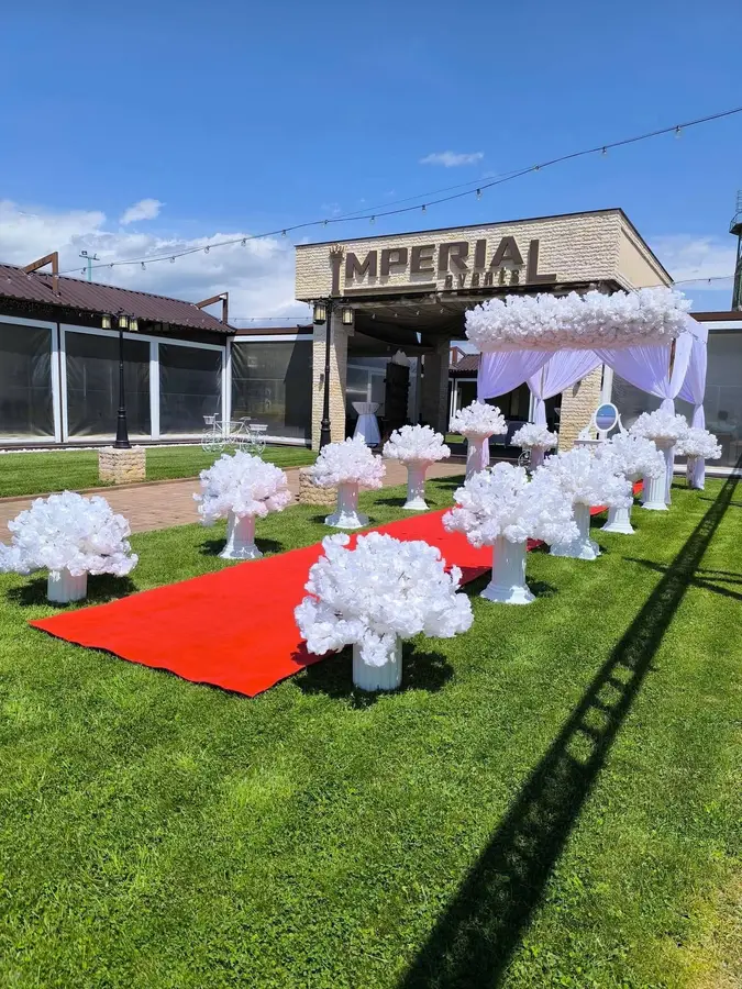 Alee de cununie în aer liber, cu covor roșu între coloane cu flori albe, la intrarea în locația Imperial Events