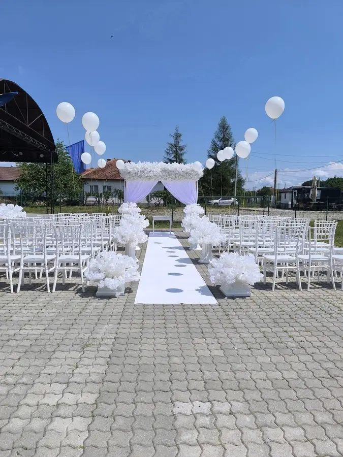 Ceremonie de cununie în aer liber, cu scaune albe Chiavari, alee cu covor alb și arcadă florală cu draperii lavandă