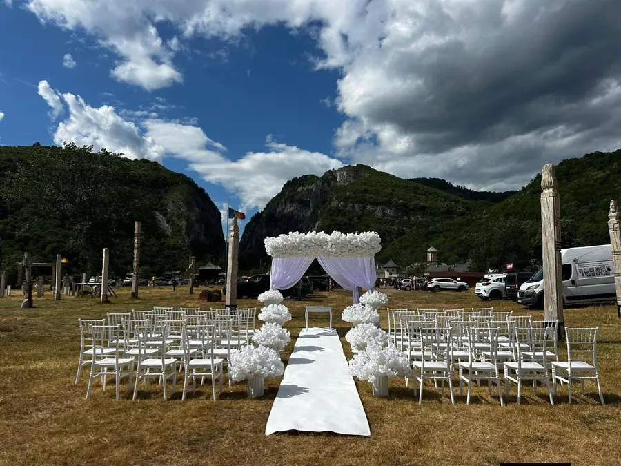 Arcadă florală albă și alee cu covor alb la o cununie în aer liber, cu fundal de munți verzi