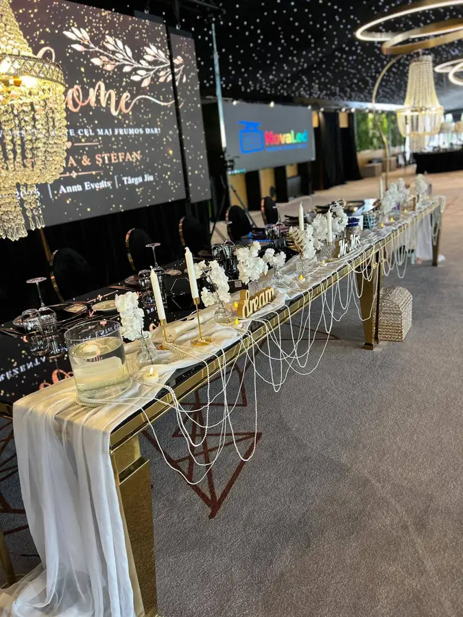 Sală de evenimente în negru cu auriu, cu panou Anna Events Welcome, masă lungă, lumânări și ghirlande de perle